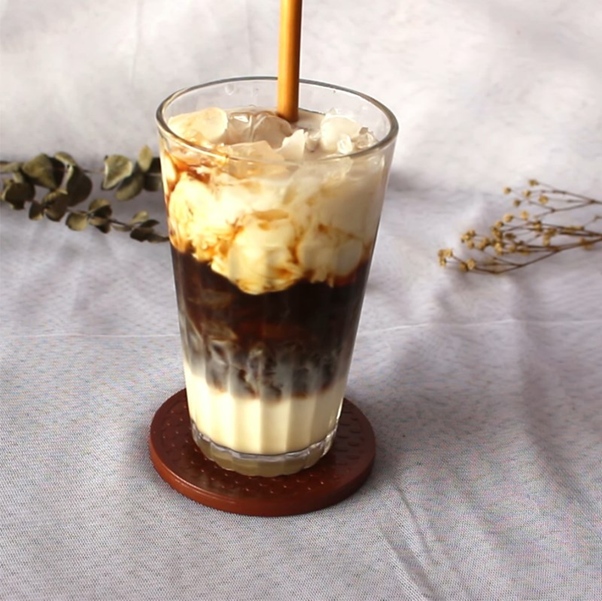 Iced layered coffee with milk in a glass, on a coaster, and a straw on a light background.
