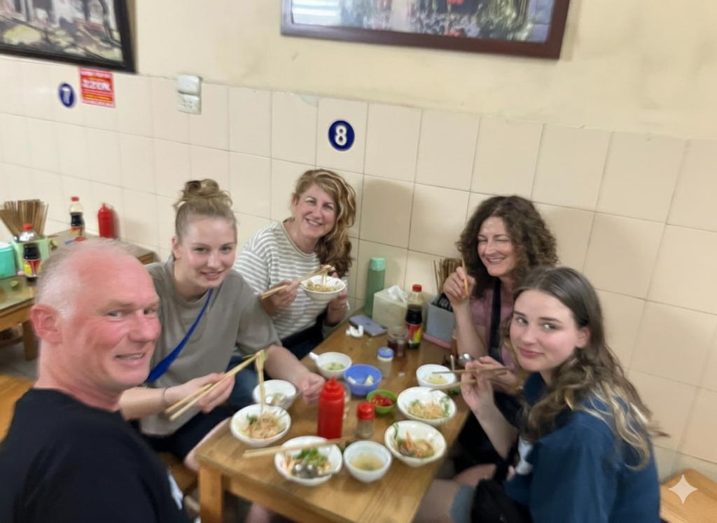 Five people enjoying a meal at a small, casual restaurant with bowls and chopsticks.