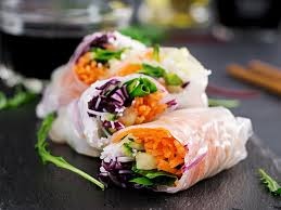 Three fresh spring rolls filled with vegetables on a slate surface.