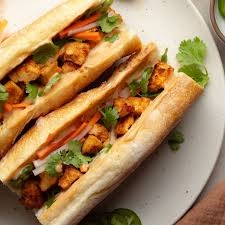 Two bánh mì sandwiches with tofu, vegetables, and cilantro on a white plate.