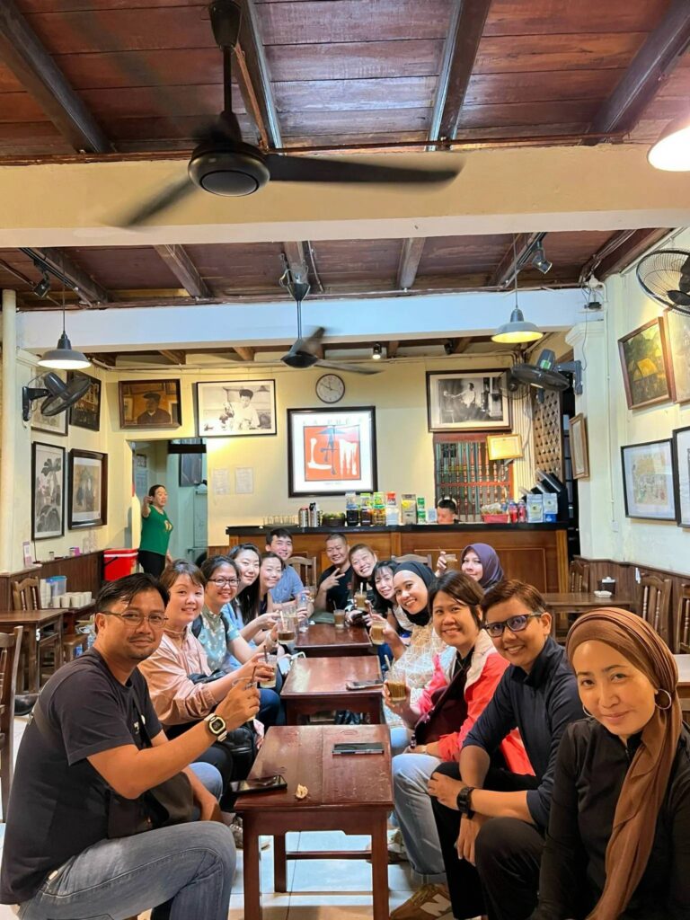 Group of people smiling and holding drinks in a cozy cafe with wooden decor.