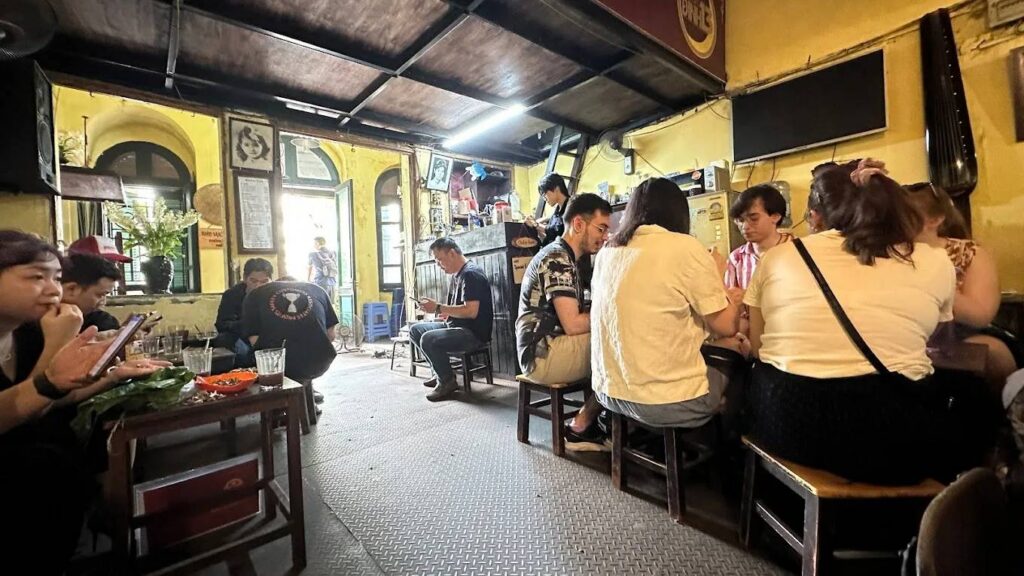 People sitting at tables inside a cozy café with yellow walls.