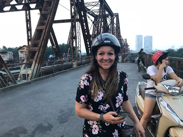 Smiling woman with helmet on bridge, holding phone.