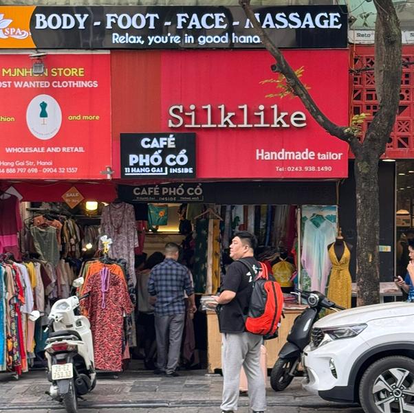 Street with clothing store and massage signs, mannequins, and parked scooters.