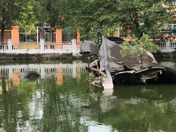 Wreckage of an aircraft submerged in a pond with trees in the background.