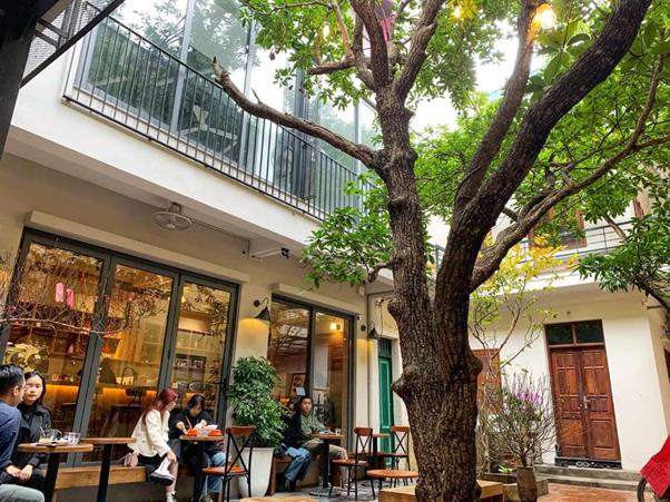 People sitting at an outdoor cafe with trees and a two-story building.