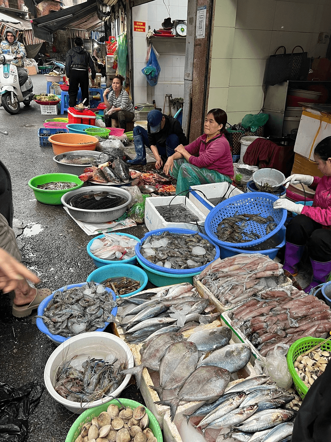 Street market with vendors selling various seafood items in bowls and baskets.