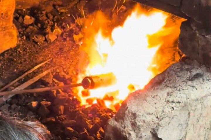 Person working with fire in a forge, with glowing flames and tools visible.