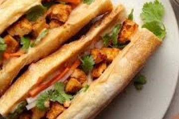 Two bánh mì sandwiches with tofu, vegetables, and cilantro on a white plate.