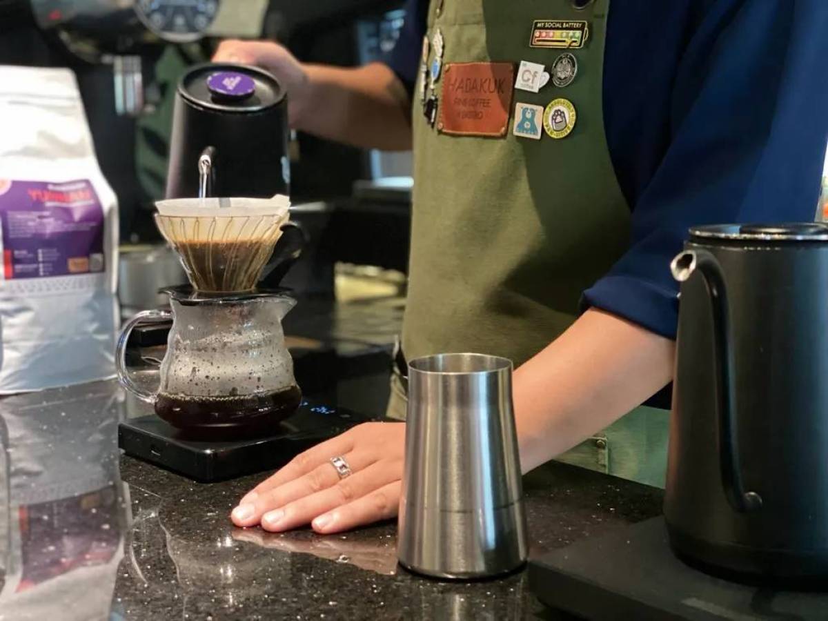 Barista making pour-over coffee at a counter with kettle and glass carafe.