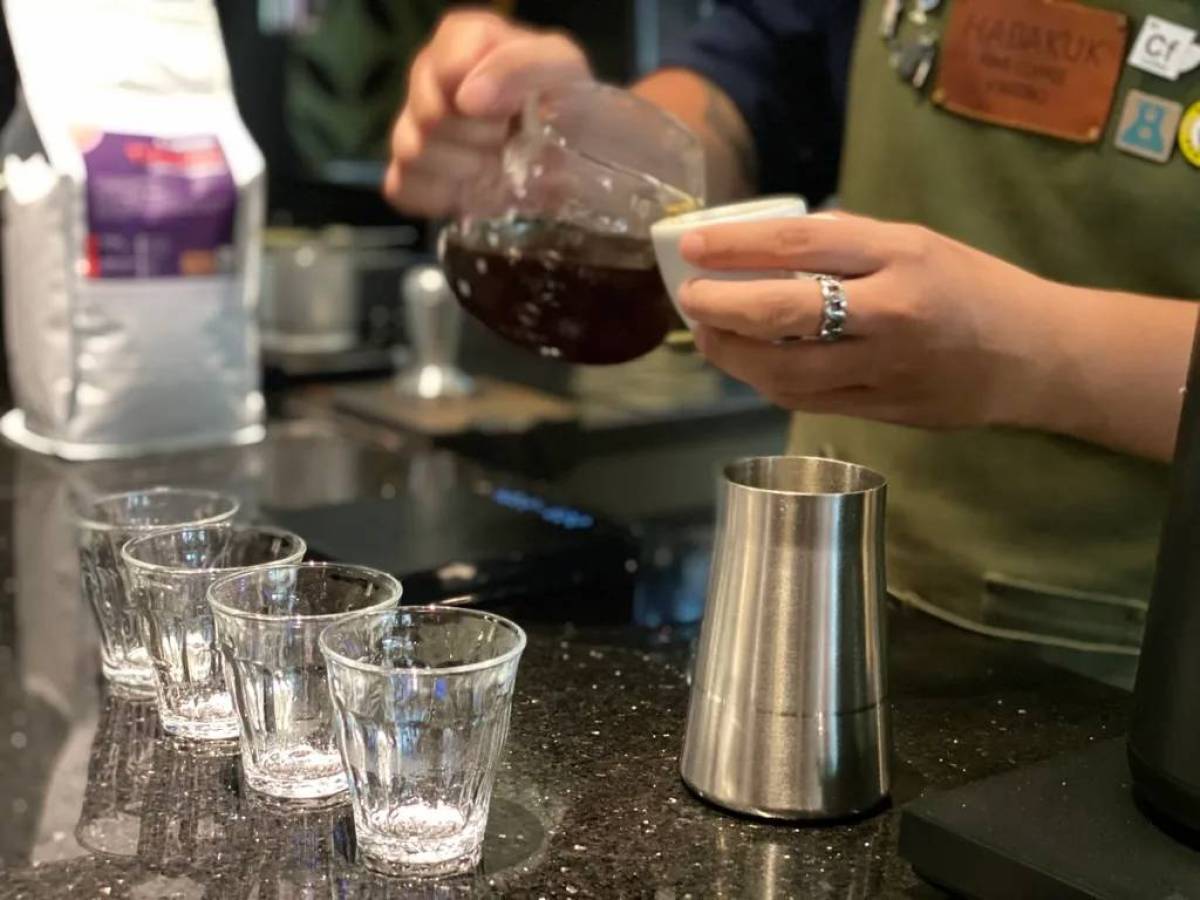 Person pouring coffee into a cup with glasses and a metal pitcher nearby on a counter.