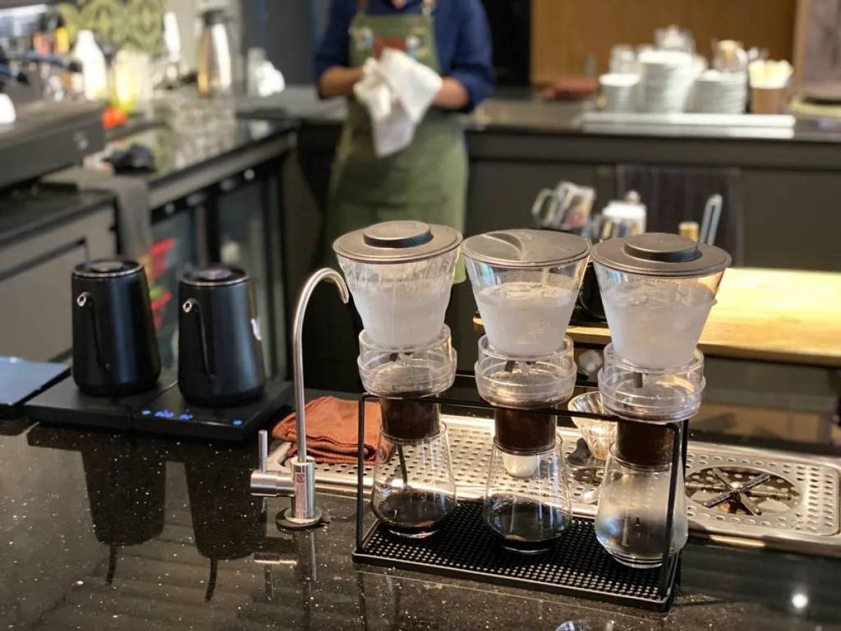 Coffee drip station with three glass brewers and black kettles on a countertop.