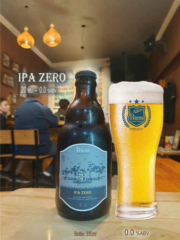 A bottle and glass of IPA Zero beer on a table in a cozy bar setting.