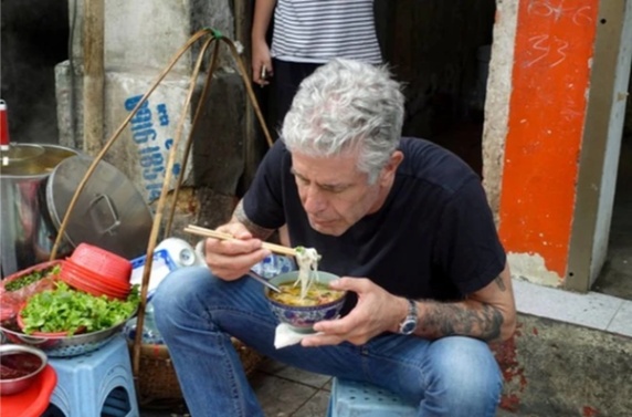 Person eating noodles with chopsticks at a street food stall.