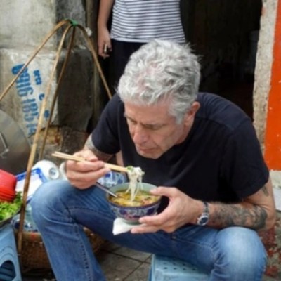 Person eating noodles with chopsticks at a street food stall.