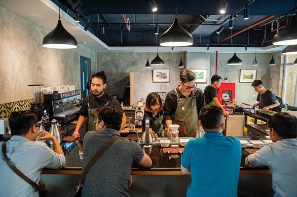Baristas serving customers at a busy coffee shop with a modern interior.