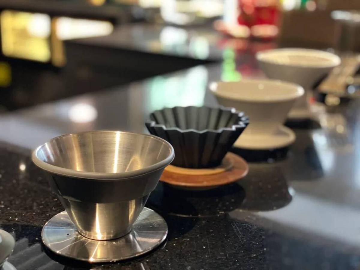 Four coffee drippers on a counter, including metal, black ceramic, and white ceramic models.