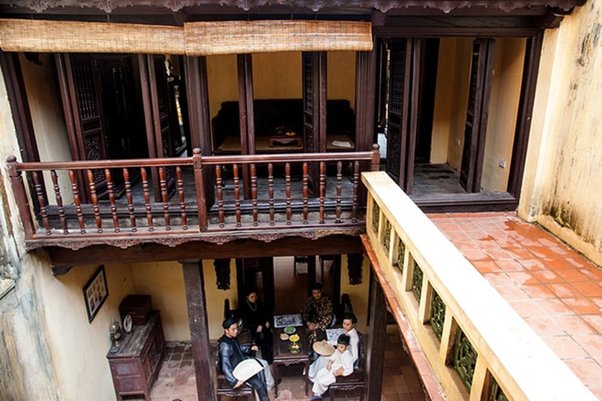 Aerial view of people sitting in a courtyard of a traditional house with wooden balcony.