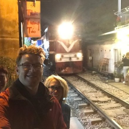 Three people take a selfie near a railway track with an oncoming train at night.
