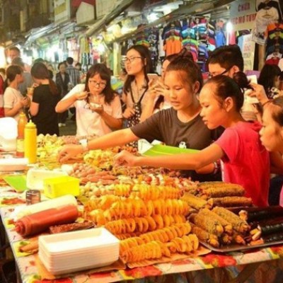 People buying and selling street food at a bustling market stall.