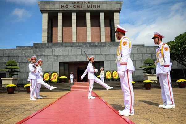 Guards in white uniforms perform at Ho Chi Minh Mausoleum, Hanoi, on a red carpet.