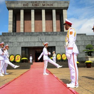 Guards in white uniforms perform at Ho Chi Minh Mausoleum, Hanoi, on a red carpet.