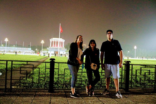 Three people stand in front of illuminated building with flag at night.