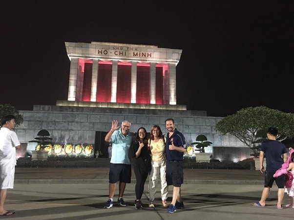 Four people posing in front of the illuminated Ho Chi Minh Mausoleum at night.