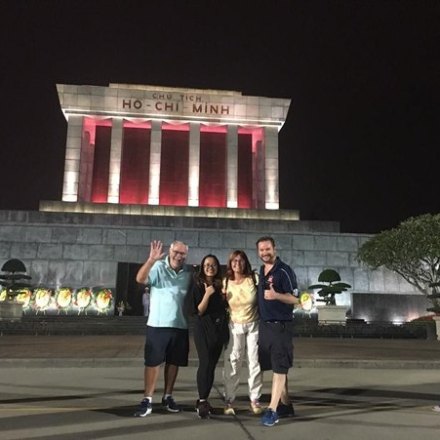 Four people posing in front of the illuminated Ho Chi Minh Mausoleum at night.