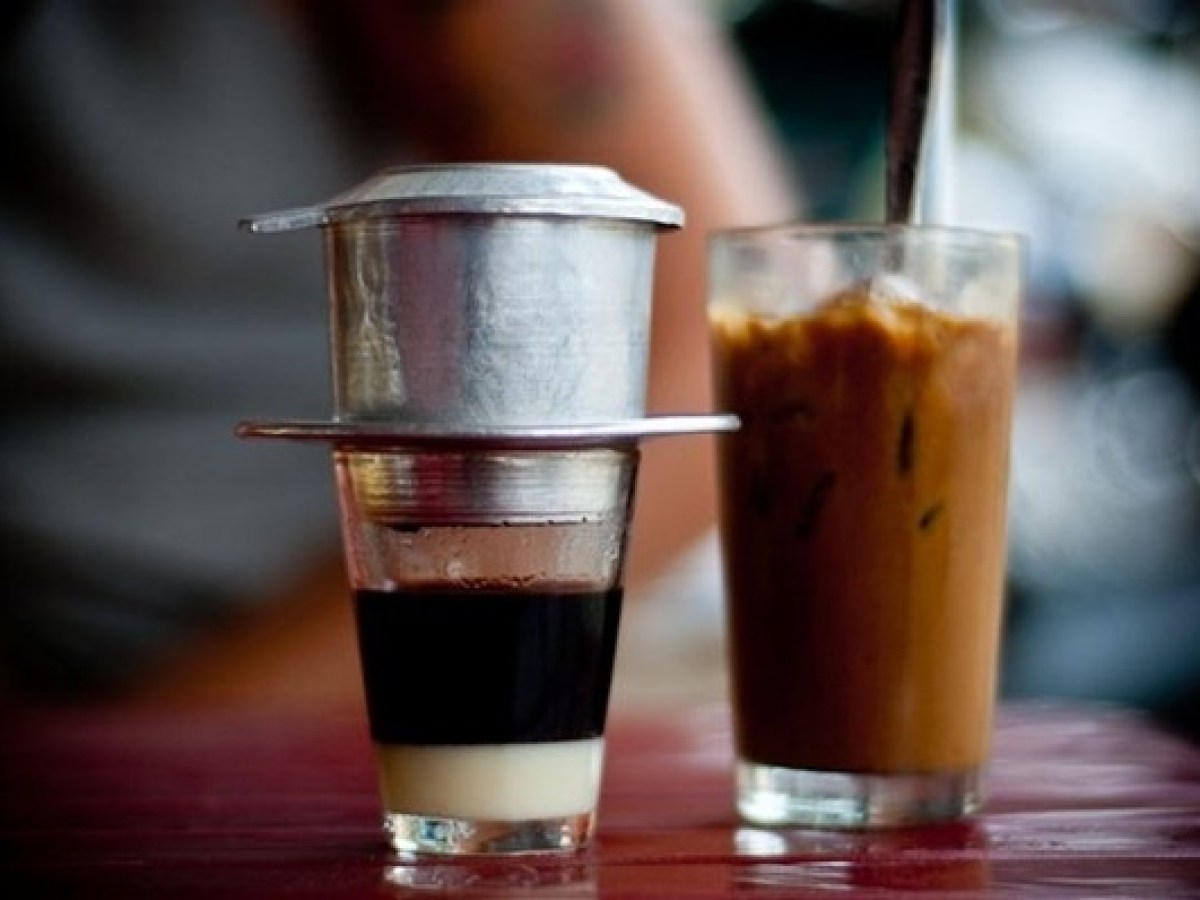 Vietnamese coffee brewing beside a glass of iced coffee on a table.