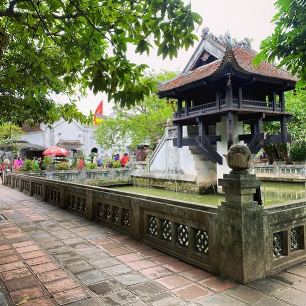 Ancient pavilion with red roof over pond, surrounded by trees and stone walkway.