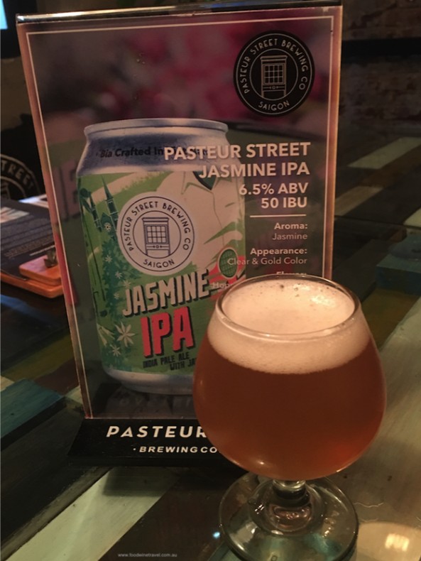 Glass of Jasmine IPA beer in front of branded sign describing its aroma and appearance.