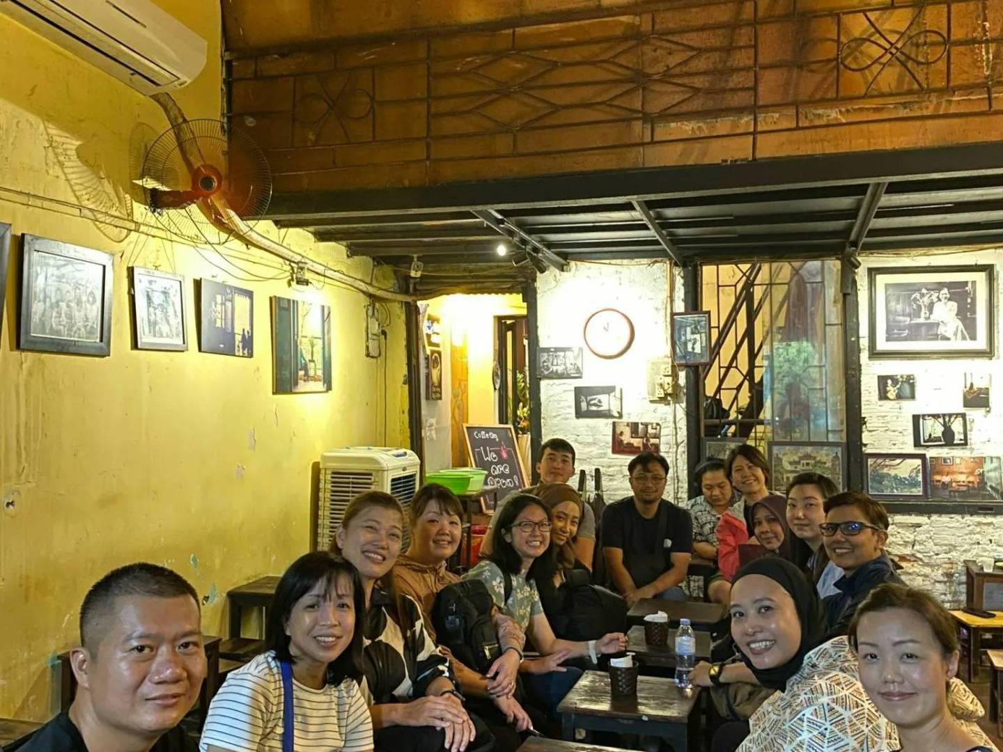 Group of people sitting closely in a dimly lit cozy cafe with vintage decor.