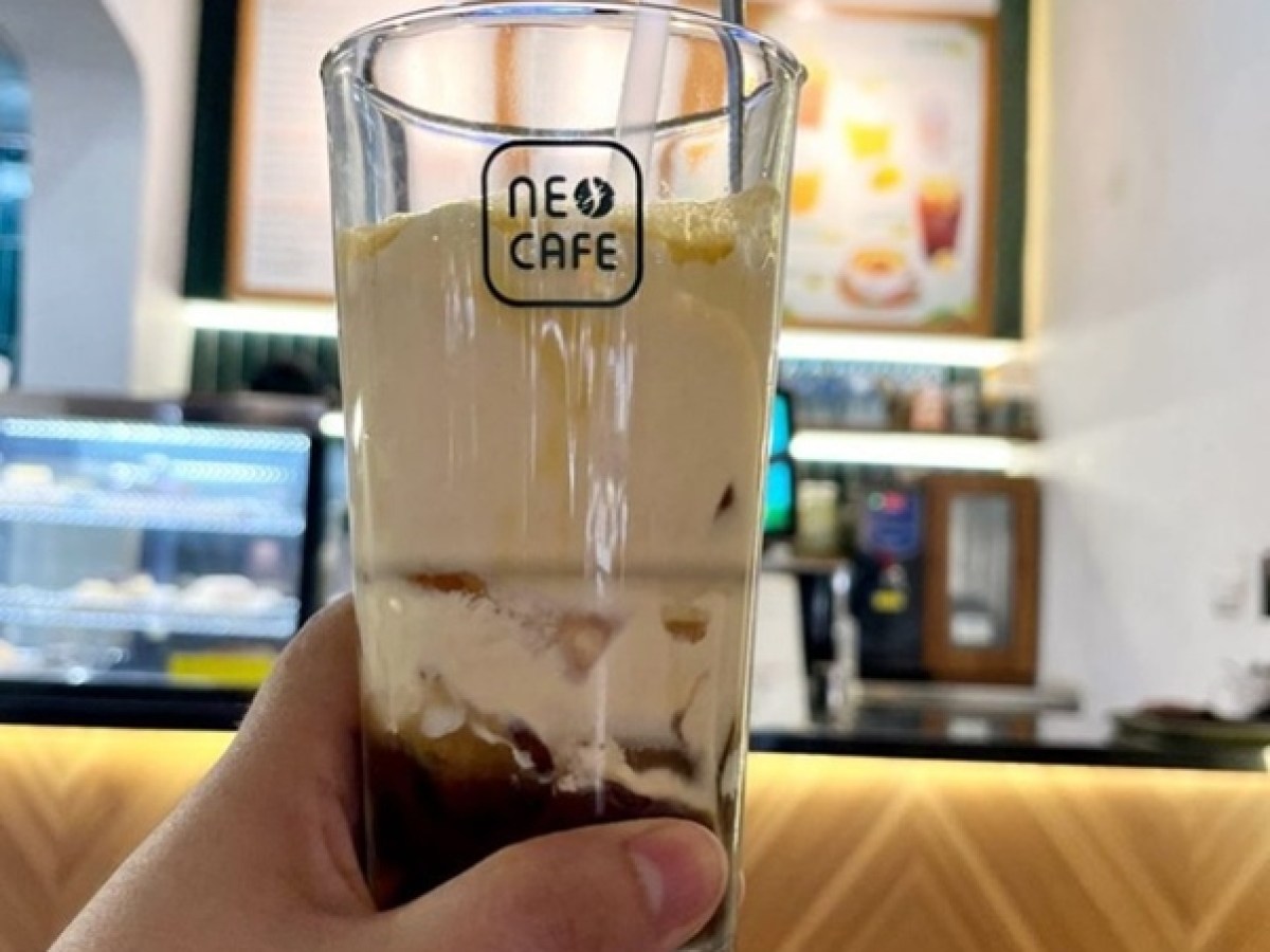 Hand holding a tall glass with iced coffee and cream in a café setting.