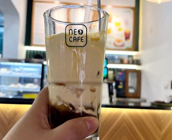 Close-up of a hand holding a glass of iced coffee in a café setting.