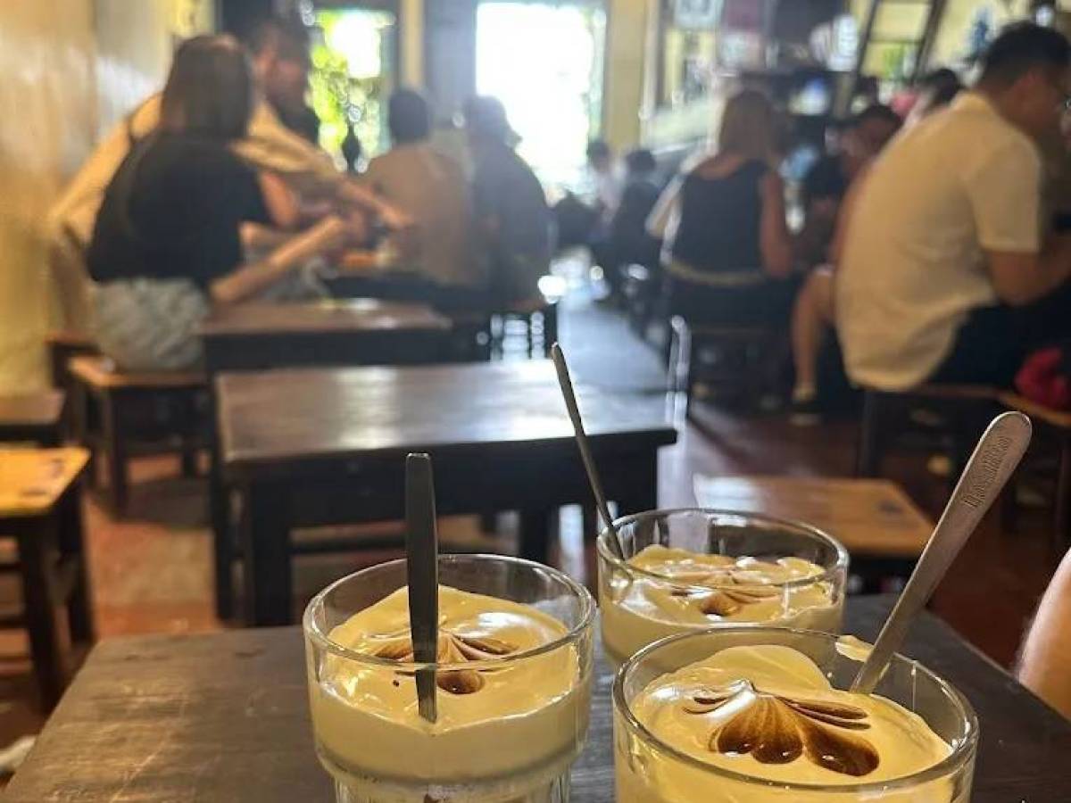 Three glasses of egg coffee with spoons on a table in a busy cafe.