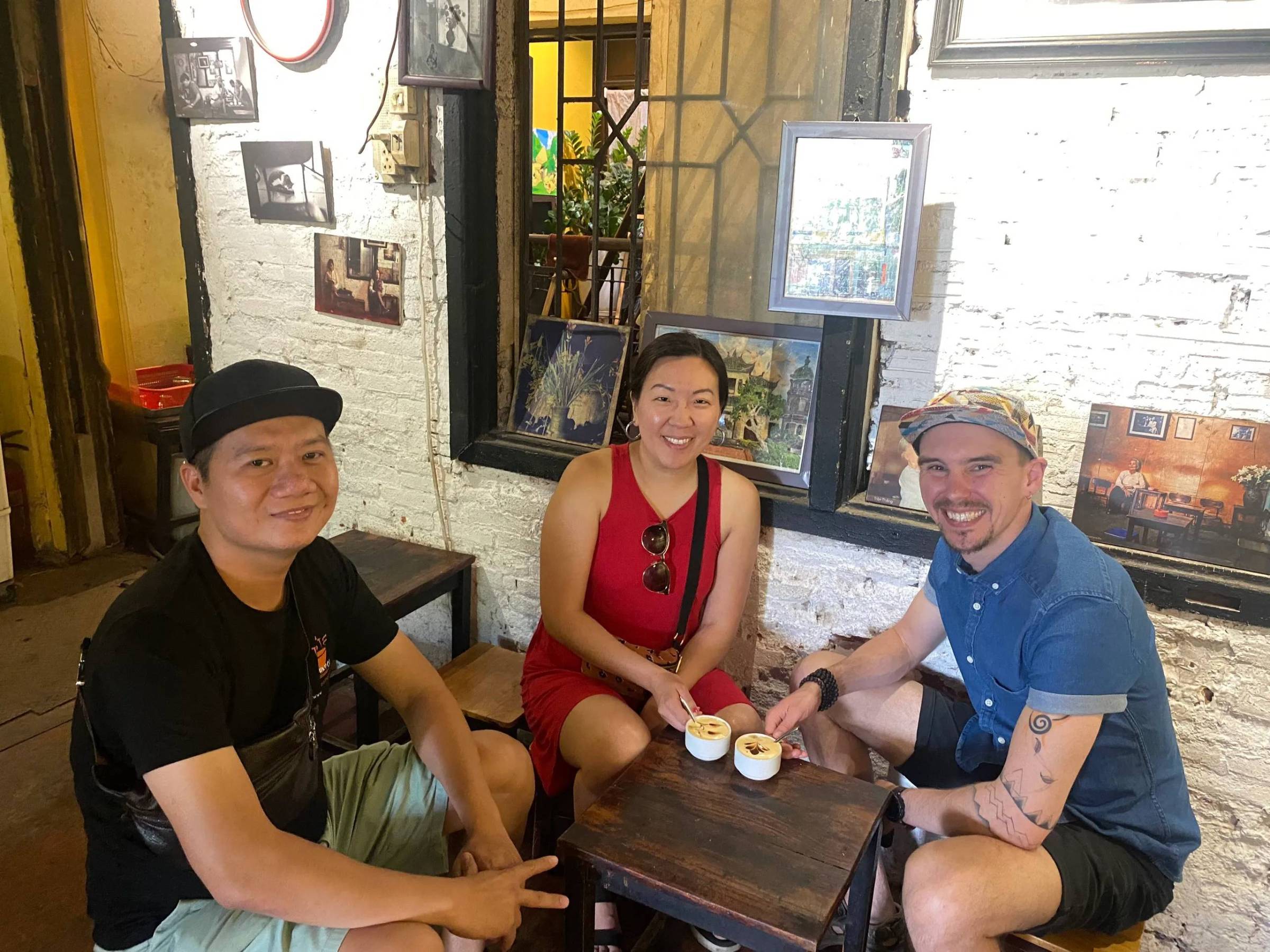 Three people sitting at a café table with coffee, smiling at the camera.