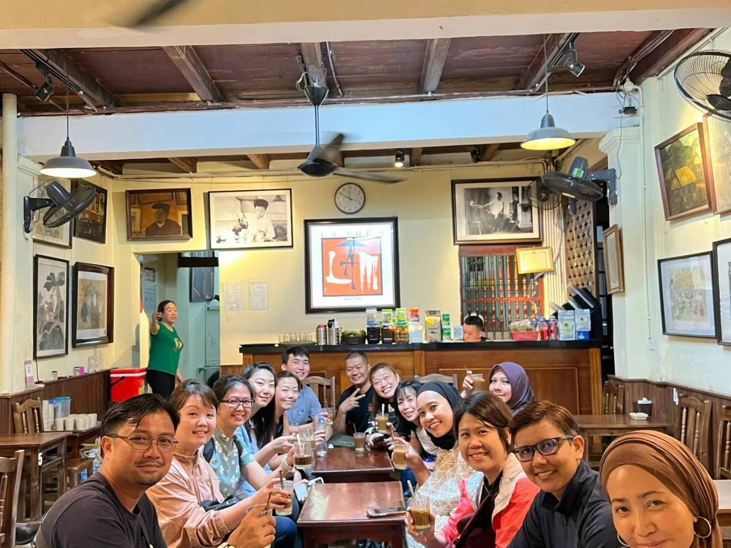Group of people smiling and holding drinks in a cozy cafe with wooden decor.