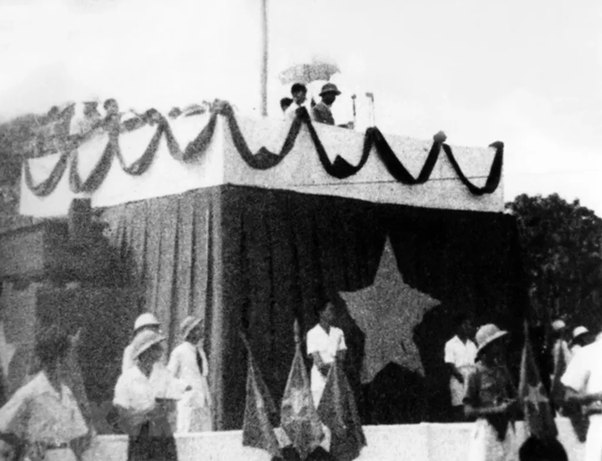 Historical photo of people on decorated stage with star banner and flags.