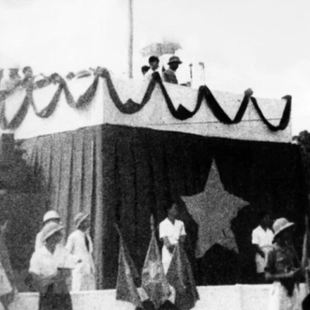 Historical photo of people on decorated stage with star banner and flags.