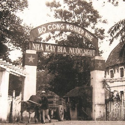 Old photo of brewery entrance with gate, trees, and cart pulled by ox and man.