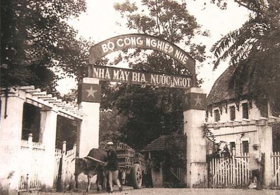 Old photo of brewery entrance with gate, trees, and cart pulled by ox and man.