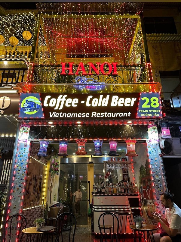 Colorful Vietnamese restaurant with bright lights, coffee and beer sign, and outdoor seating.