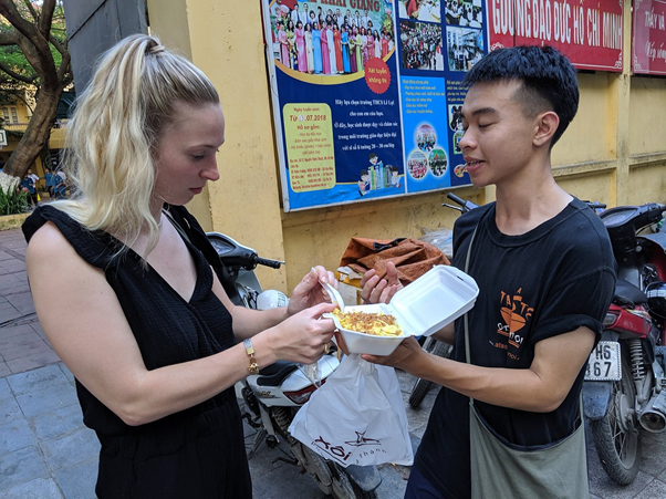 Two people sharing food from a takeout container near parked motorcycles.