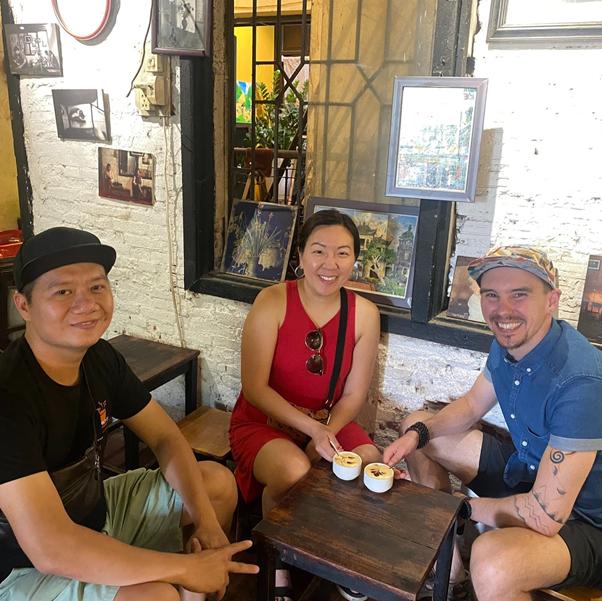 Three smiling people sitting at a small table with coffee cups.