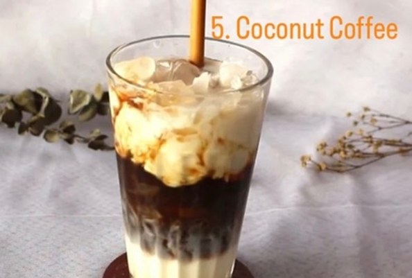 Glass of layered coconut coffee with a straw on a table.