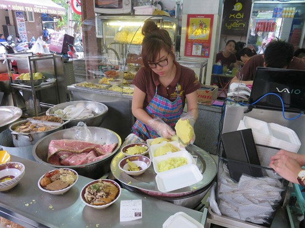Woman in apron preparing food at a busy street food stall.