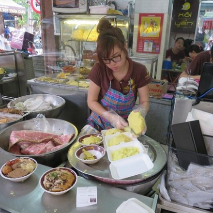 Woman in apron preparing food at a busy street food stall.