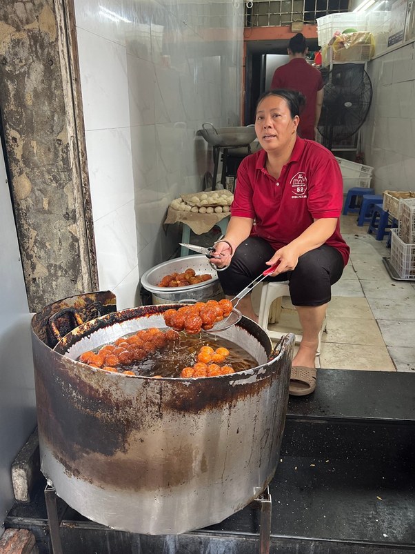 Person frying food balls in a large pot of oil in a small kitchen.