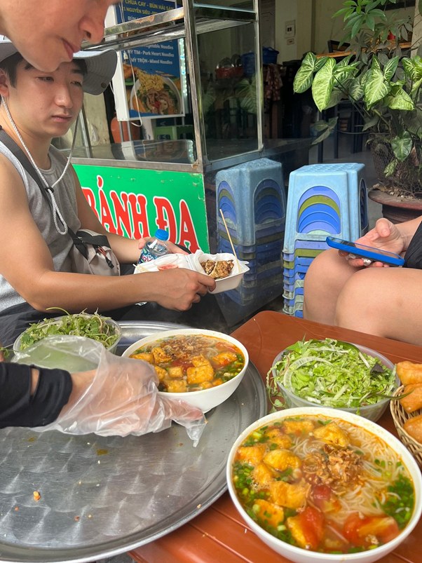 People enjoying noodle soup and salad at a street food stall.